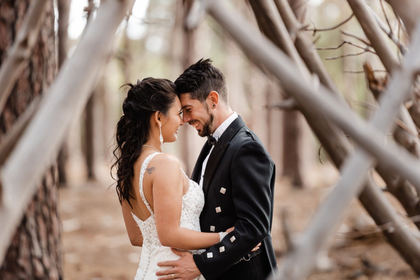 The branches of a pine tree frame a young couple laughing and hugging in a forest in Wannerroo Pines, WA.