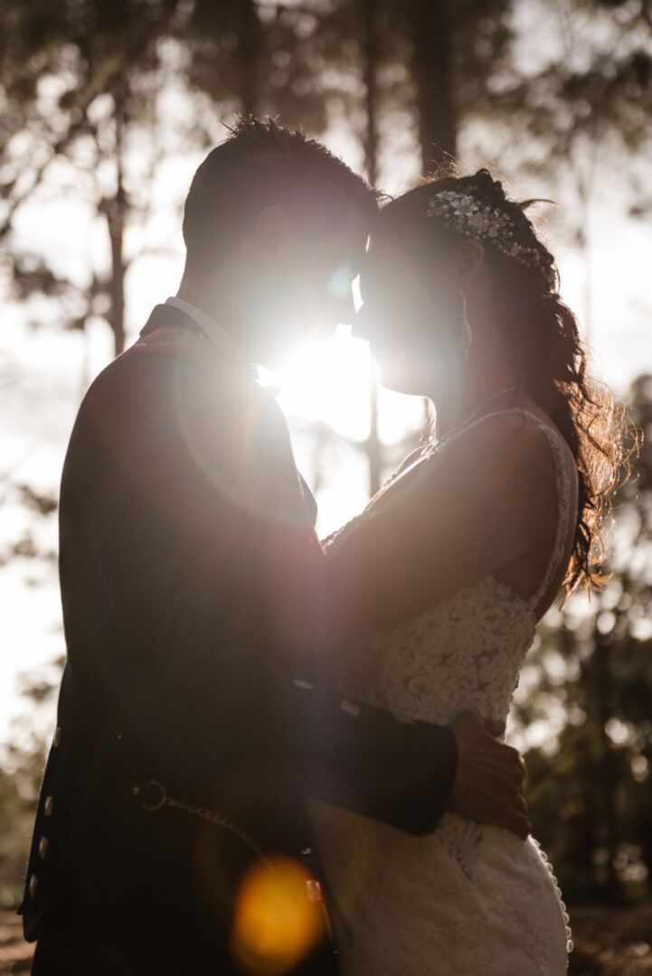 The groom and the bride hold tight and touch their heads together in a pine forest in Wanneroo Pines, WA.