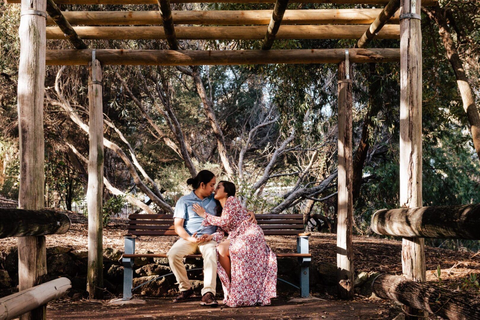 A couple kisses while sitting on a bench in a park in Perth.