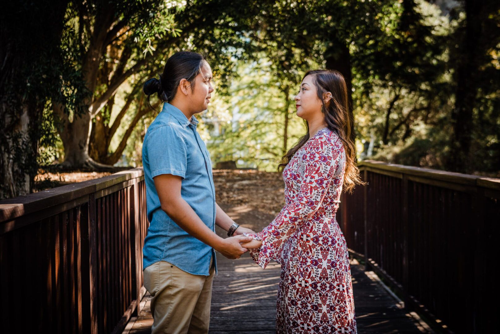 A man and a woman hold hands while looking at each other on a wooden bridge in a park in Perth, WA.