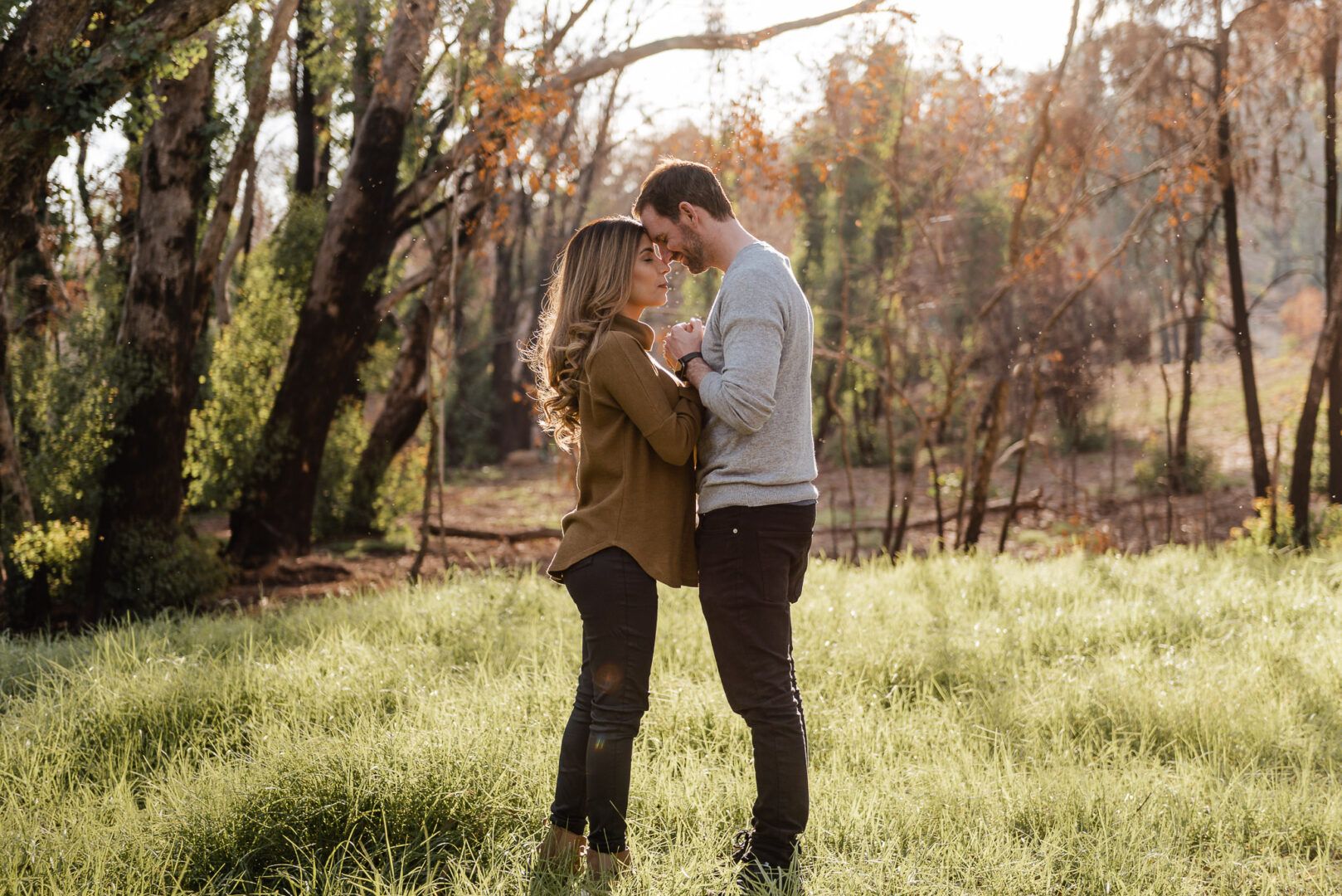 Two lovers stand in front of each other in a field at sunset