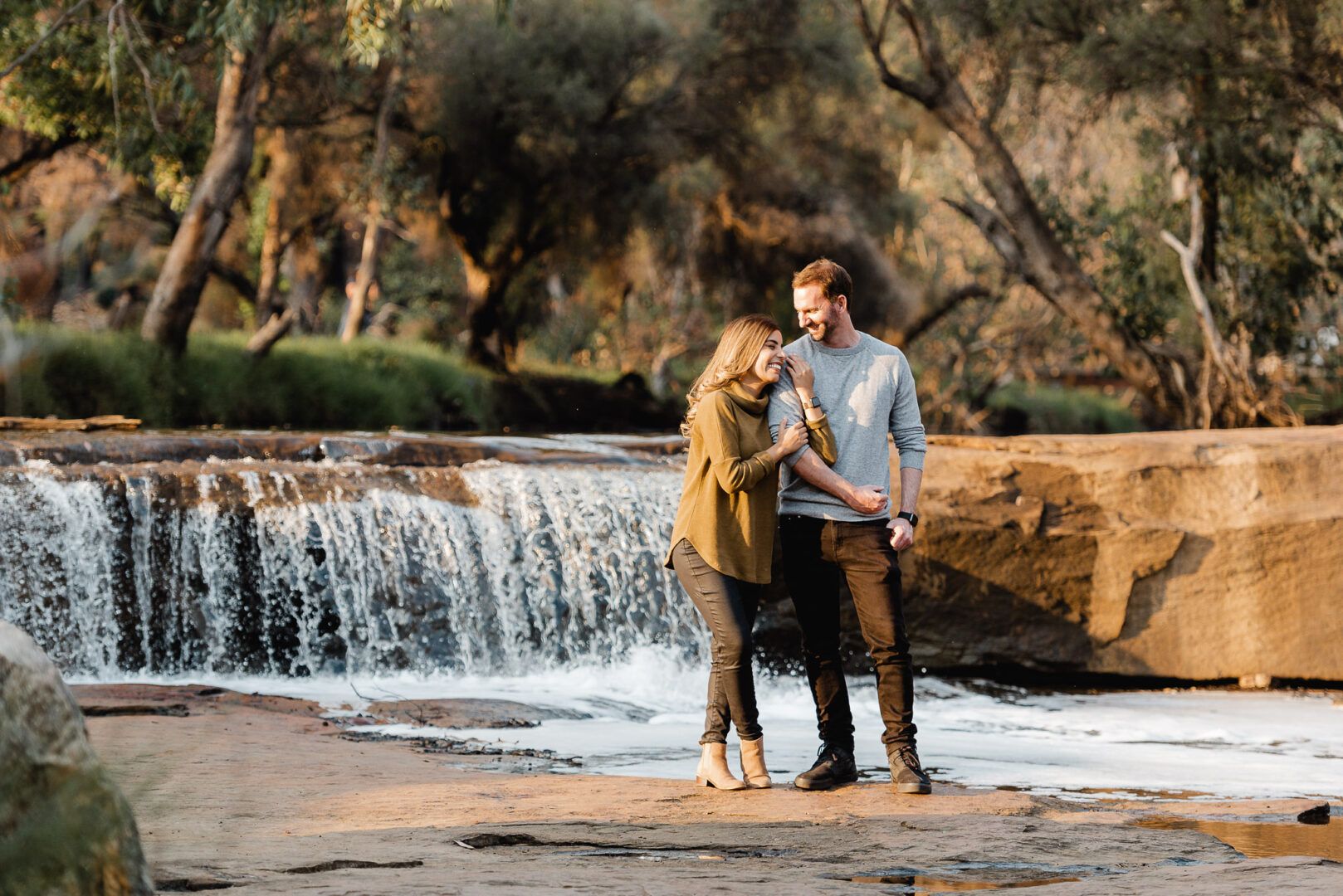 Boyfriend and girlfriend walk together next to a waterfall during a couple photoshoot at Noble Falls
