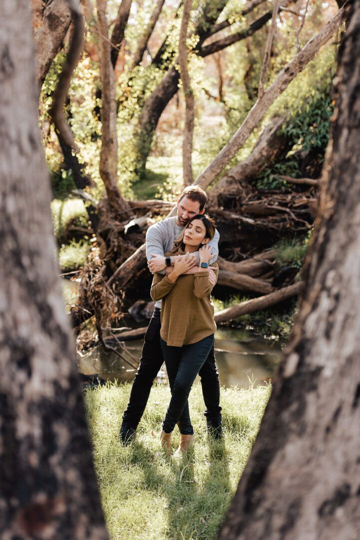 A tree frames a ccouple hugging in the background