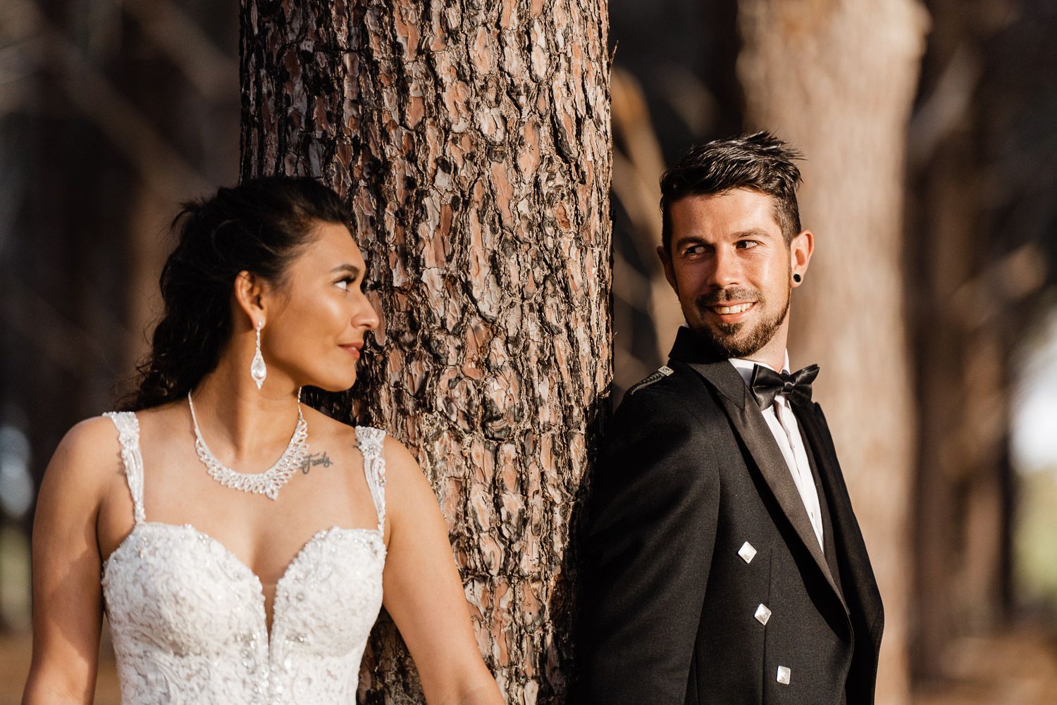 The groom looks at the bride while leaning on a pine tree in Wanneroo Pines, WA.